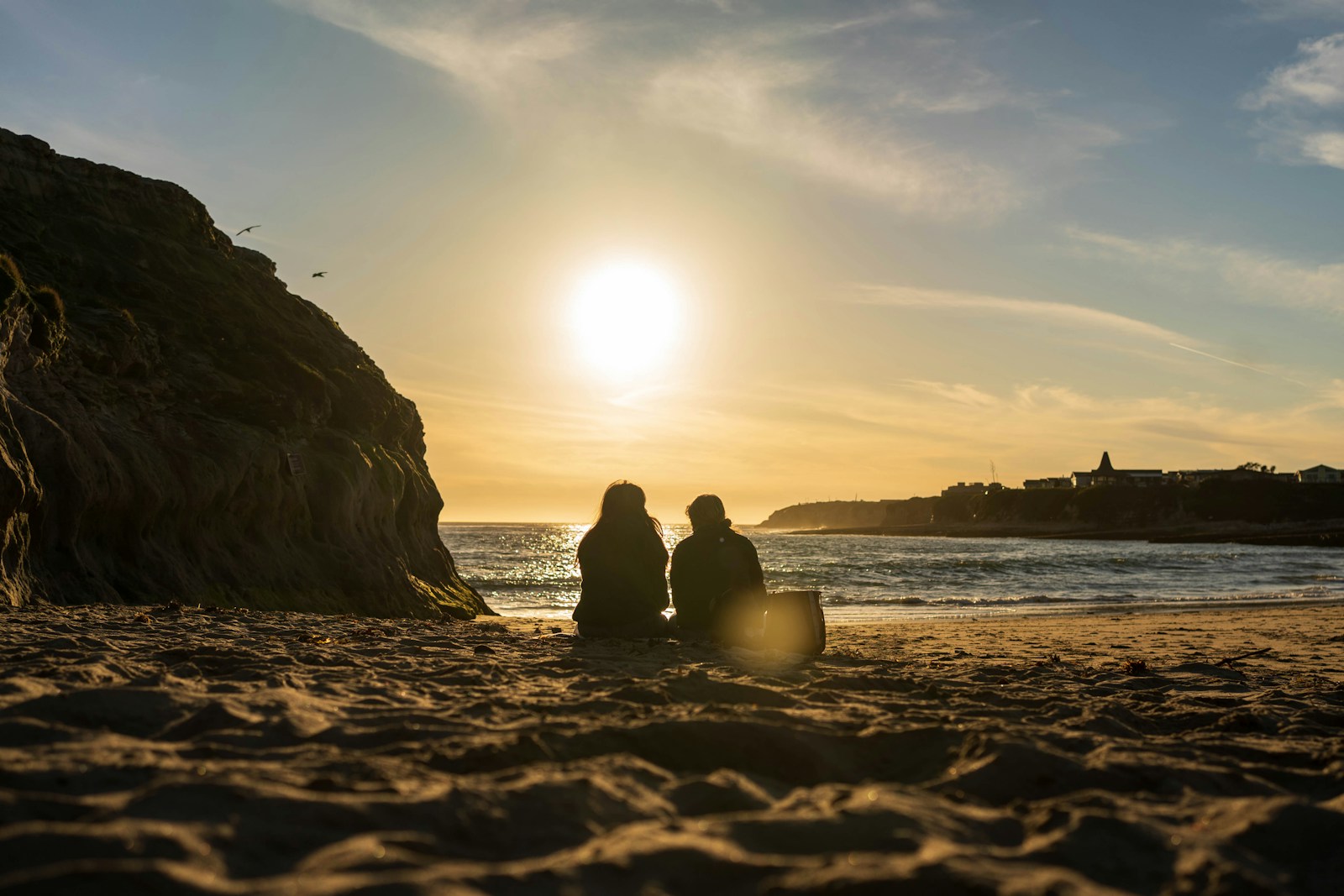 two people sitting on the beach watching the sun set